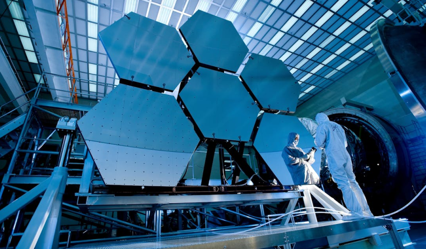 A man and woman in lab coats examining a large blue satellite